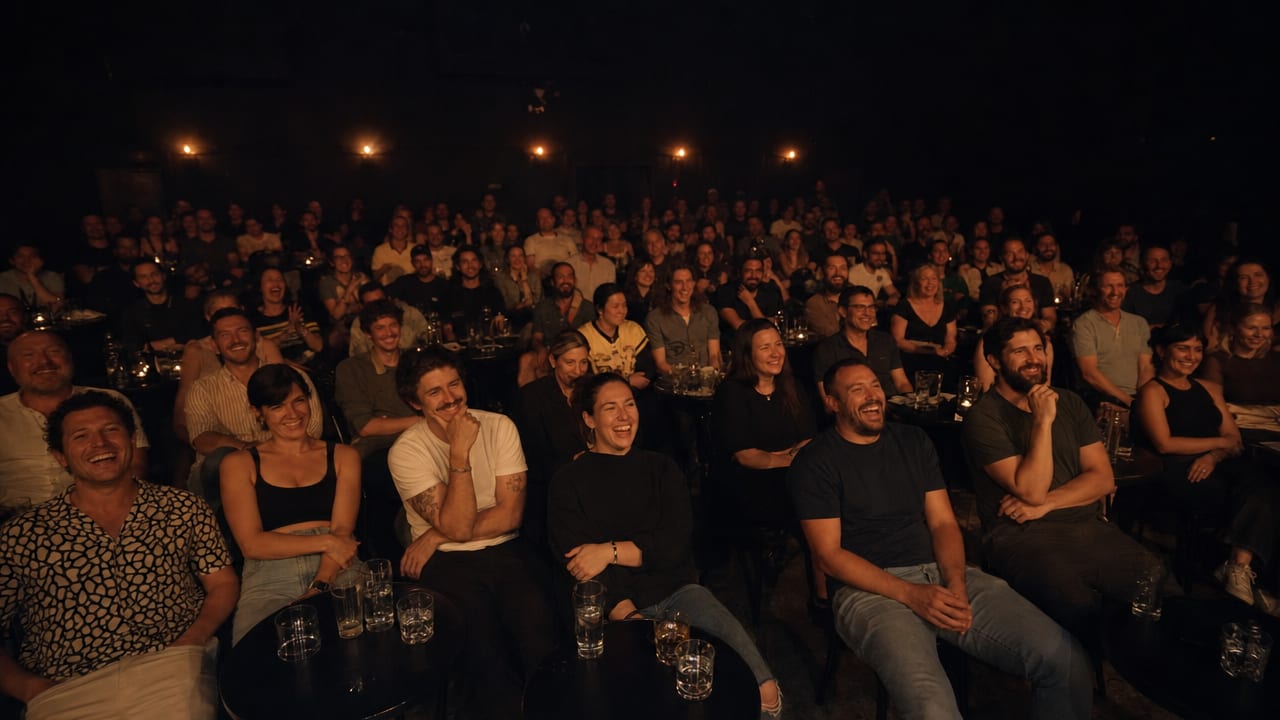 An audience in near-darkness at small round tables